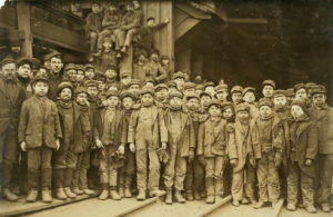 Black and white photograph of a group of around 50 young boys, dressed for work in a coal mine