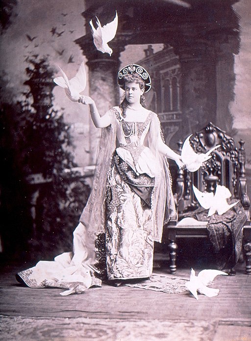 Black and white photograph of a woman wearing an elaborate Renaissance-inspired dress, surrounded by doves