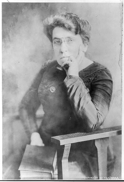 Black and white portrait of Emma Goldman, resting elbow on arm of a chair