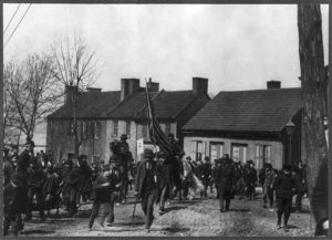 Image of Coxey's Army in front of building, with flag bearer in center