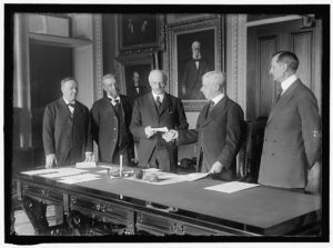 Black and white photograph of five men standing next to a large table