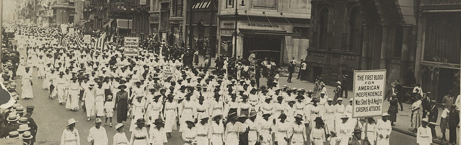 Photograph of a protest parade; sign in front reads "THE FIRST BLOOD FOR AMERICAN INDEPENDENCE Was Shed By A Negro CRISPUS ATTUCKS"