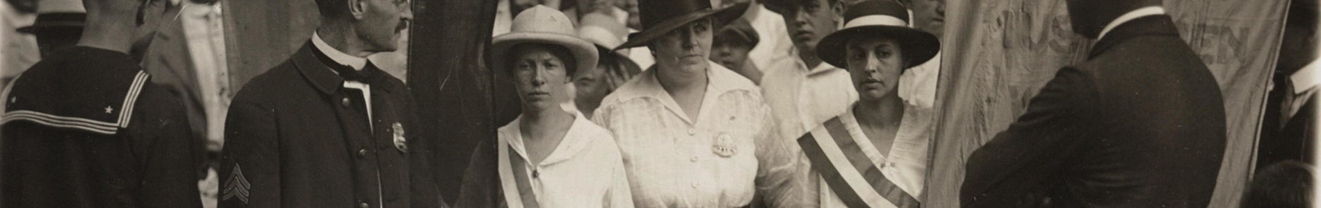 Catherine Flanagan (left) and Madeleine Watson (right) of the National Woman's Party being arrested by police officer (center) as they picket with banners in front of the White House East Gate