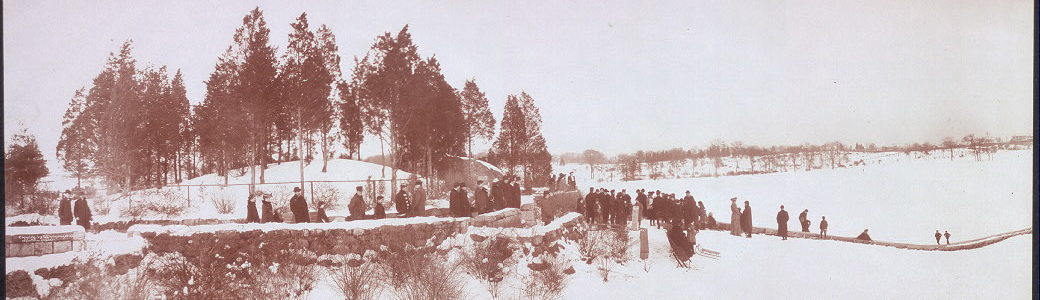 Black and white photograph of people in winter attire standing along the top of a snow-covered hill