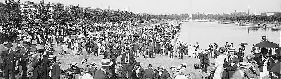 Crowd of people standing on lawn in front of Lincoln Memorial reflecting pool